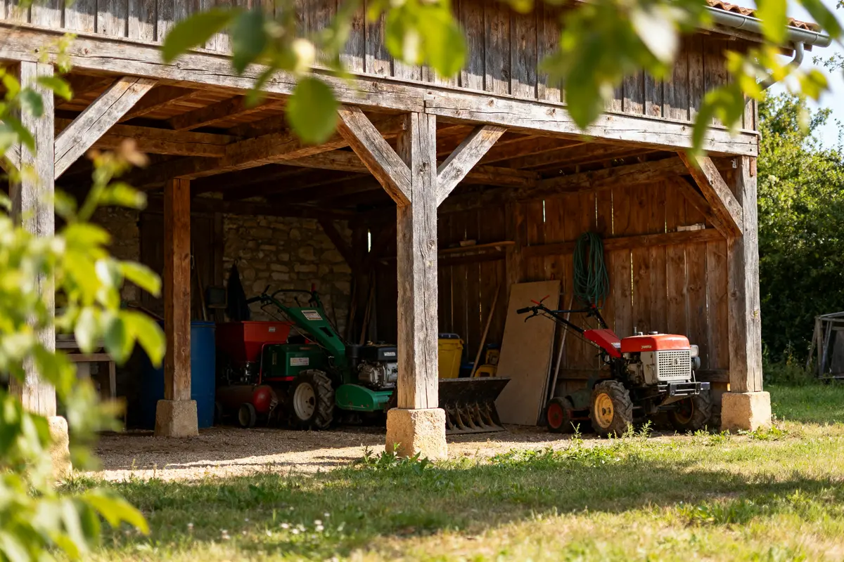 Appentis en bois avec matériel agricole rangé à l'intérieur et verdure environnante