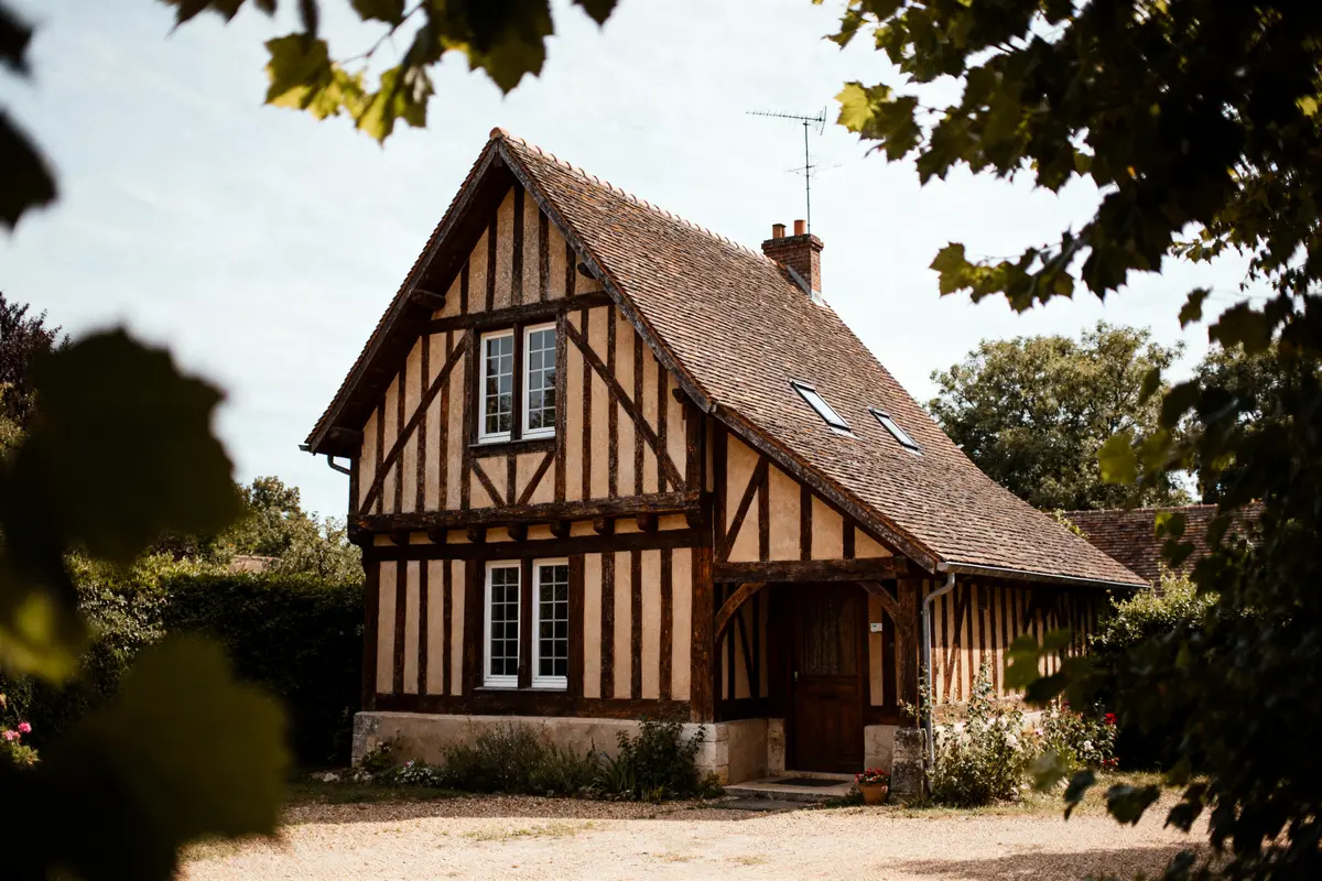 Maison traditionnelle avec colombages illustrant l'architecture tudor, entourée d'arbres verdoyants