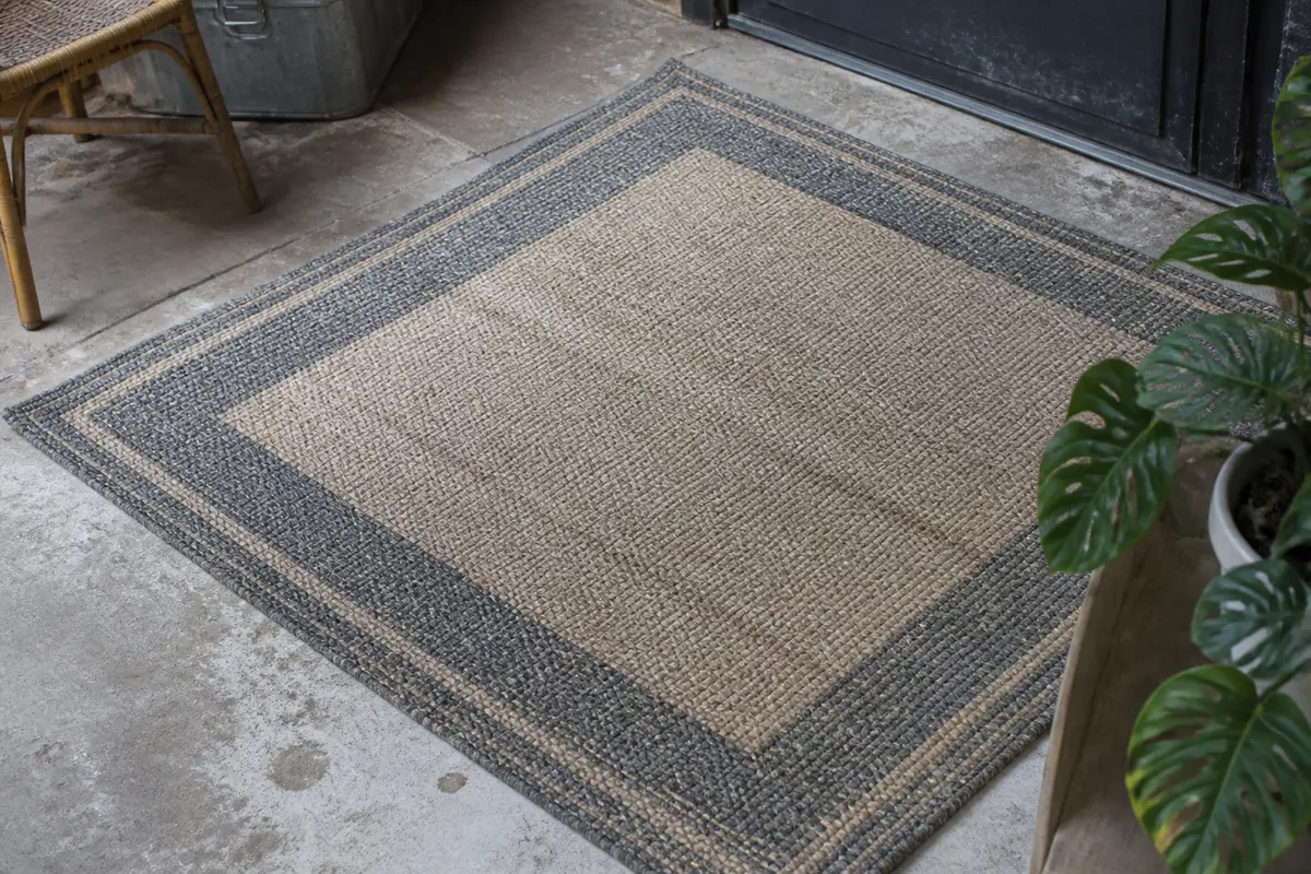Tapis style industriel beige et gris sur sol de béton à côté d'une plante verte