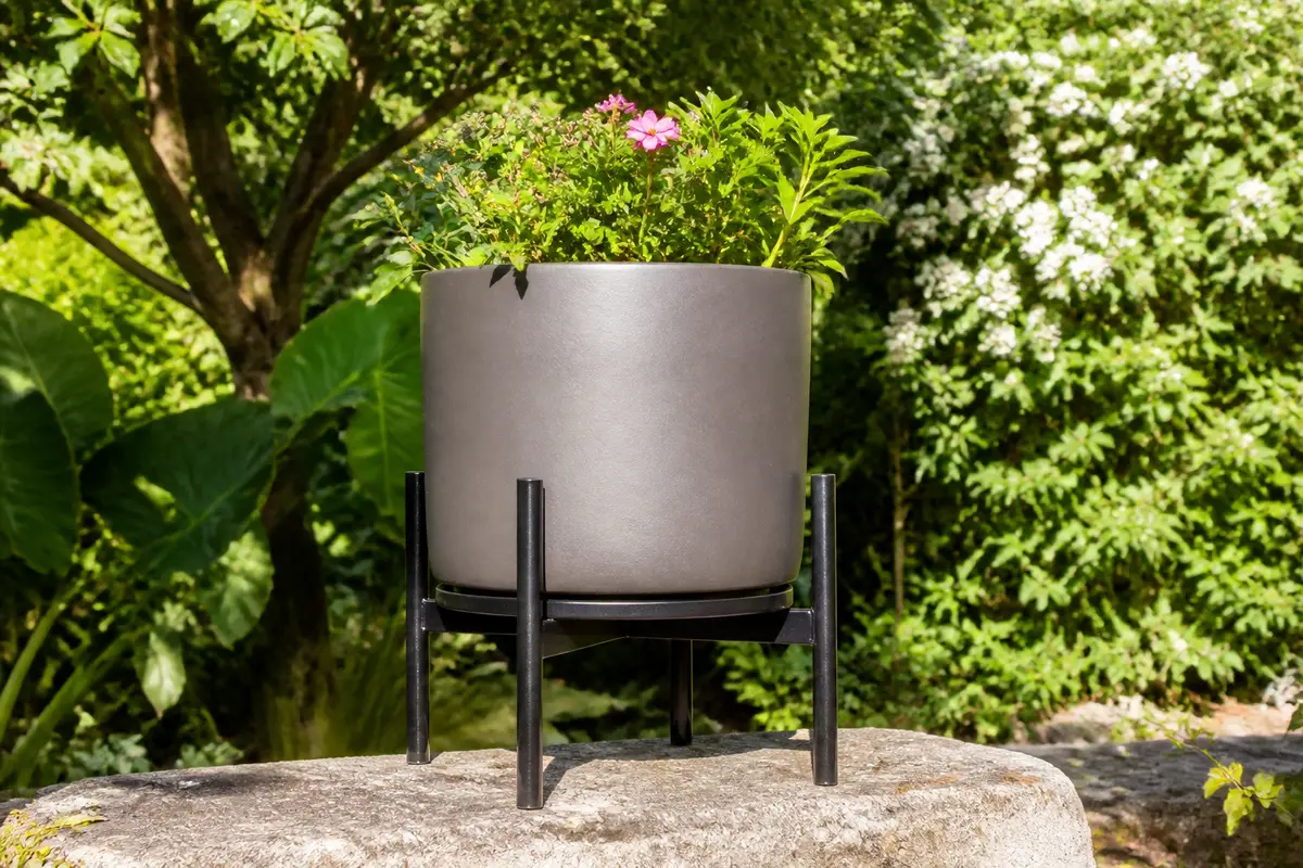 Pot de fleur sur support en métal dans un jardin verdoyant ensoleillé